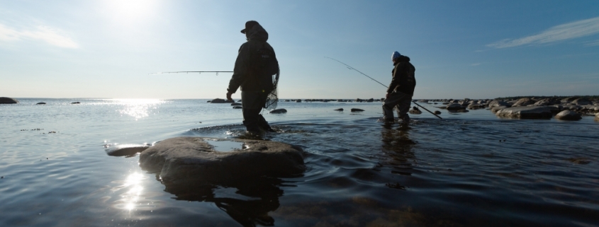 Two people holding fishing rodds wile standing i n shallow water